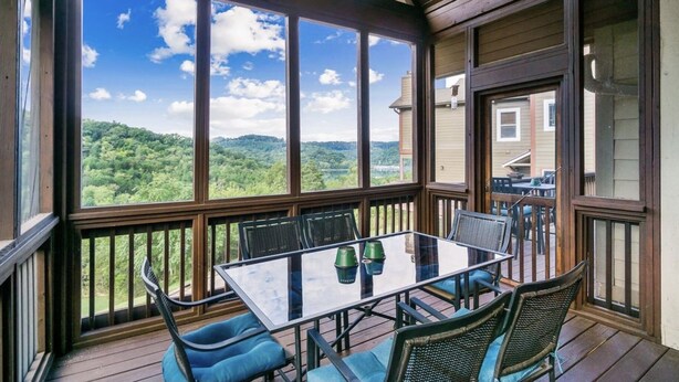 A covered outdoor area with a table and chairs, large windows offering a view of a forested landscape. - Tranquil Waters Retreat: Hot Tub, Pool & Lake Views (Smithville)