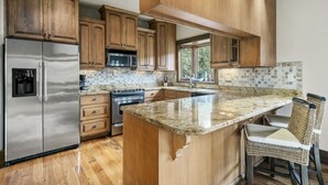 A kitchen with wooden cabinets, stainless steel appliances, a granite countertop, and a view of the outdoors. - Tranquil Waters Retreat: Hot Tub, Pool & Lake Views (Smithville)