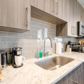 A modern kitchen with a stainless steel sink, a coffee maker, and a microwave. - Arlington Upscale Studio Apartment (Arlington)