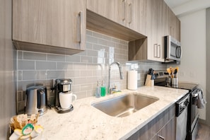 A modern kitchen with wooden cabinets, a stainless steel sink, and a microwave. - Arlington Upscale Studio Apartment (Arlington)