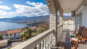 Un balcon doté d’une balustrade en pierre, offrant une vue sur un lac et le paysage urbain.