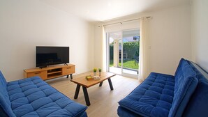 Un salon moderne doté d’un téléviseur à écran plat, de deux canapés bleus, d’une table basse en bois et d’une porte-fenêtre coulissante donnant sur un balcon.