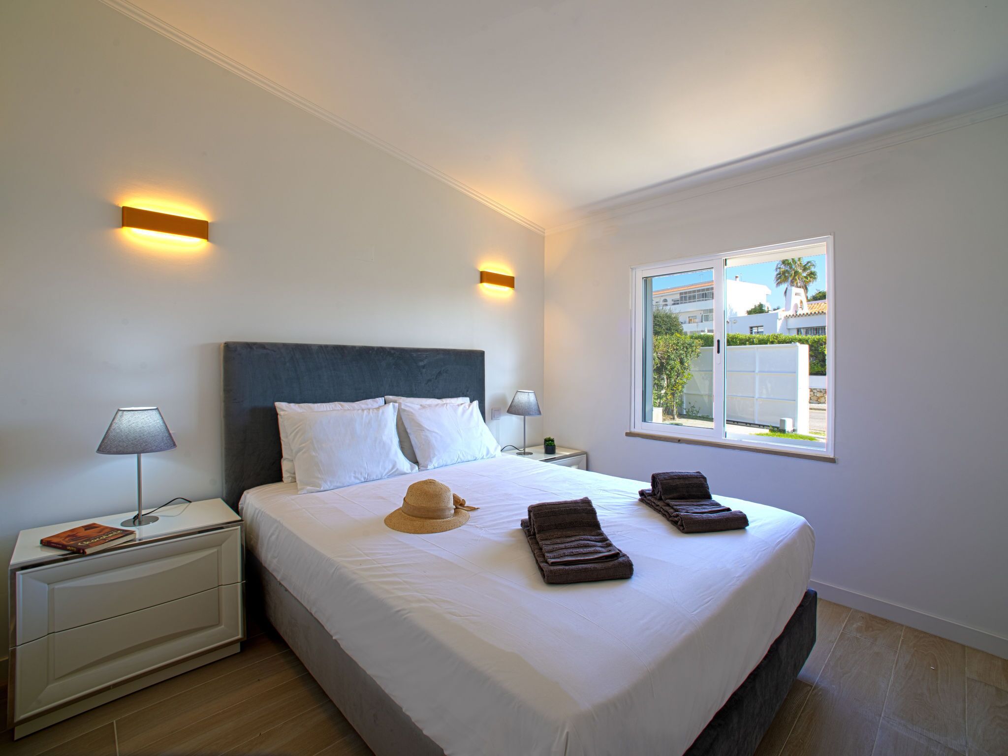 Hotelkamer met een groot bed, twee nachtkastjes, een raam met uitzicht op gebouwen en een wandlamp.