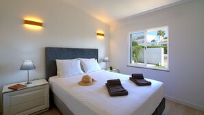 Une chambre d’hôtel avec un grand lit, deux tables de chevet, une fenêtre donnant sur des immeubles et un luminaire fixé au mur.