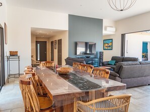 Een ruime woonkamer met een lange eettafel, comfortabele zithoeken, een moderne bank en een grote flatscreen televisie.