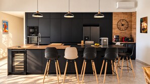 Een moderne keuken met een centraal eiland, hangende verlichting en een klok aan de muur.
