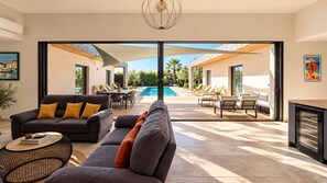 A modern living room with a large sofa, a coffee table, and a pool view.