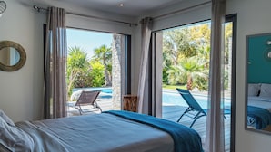 A bedroom with a bed, a view of a swimming pool, and a balcony with a chair.