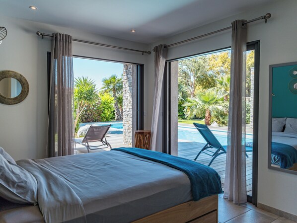 Een slaapkamer met een bed, zwembad uitzicht en een balkon met een stoel.