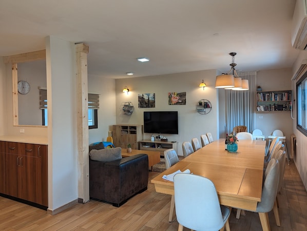 Un salon moderne avec une table à manger en bois, des sièges confortables, un téléviseur à écran plat et une bibliothèque.