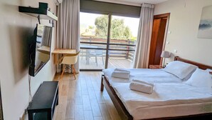Une chambre d’hôtel équipée d’un lit, d’un bureau, d’une chaise, d’une télévision et d’un balcon donnant sur la verdure.