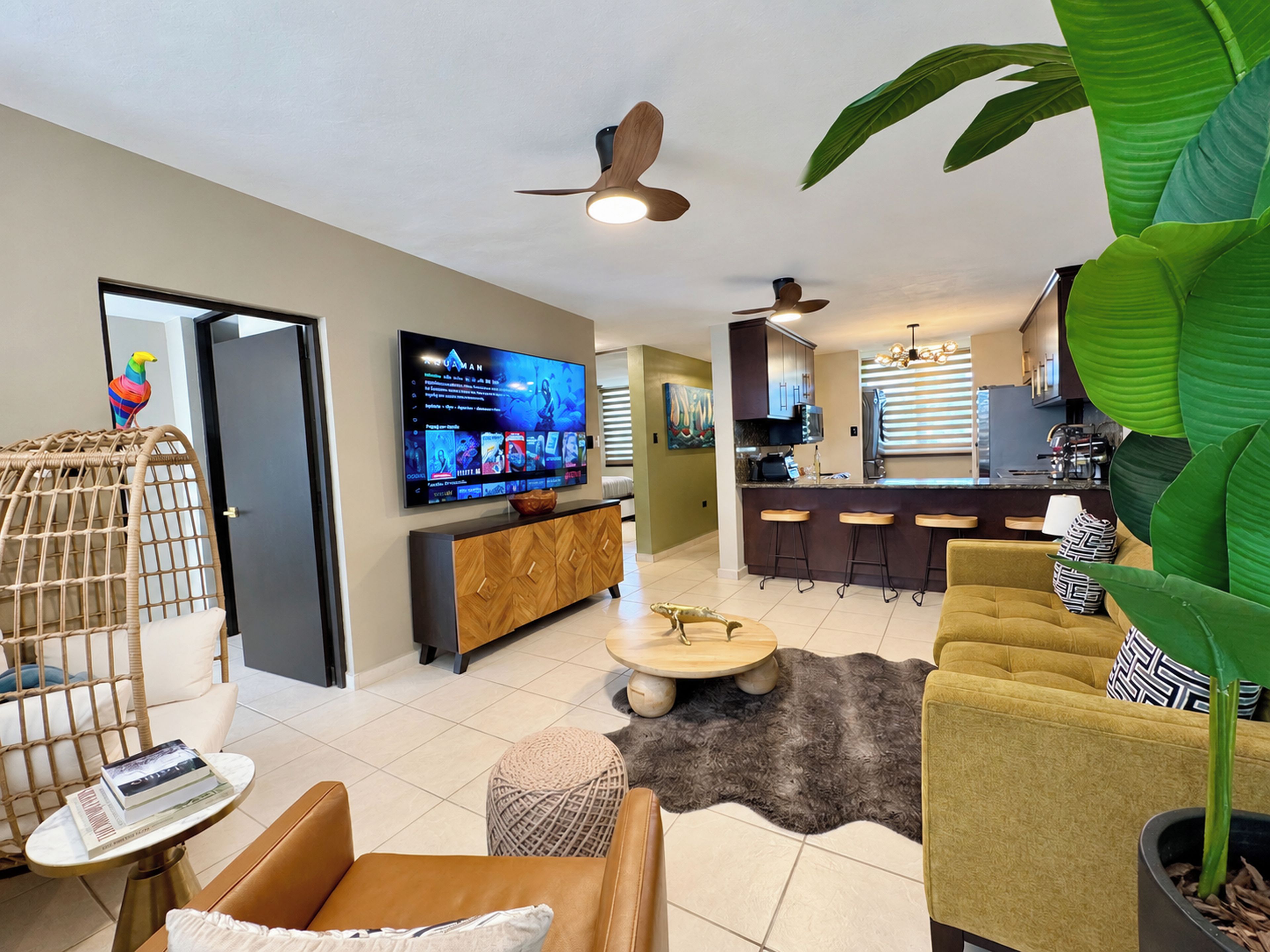 A modern living room with a television, seating area, and a kitchen in the background.