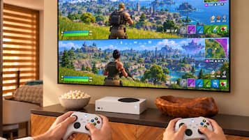 Ein Fernseher zeigt ein Videospiel mit zwei Spielern, eine Spielkonsole und eine Schüssel Popcorn stehen auf einer Theke.