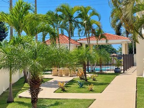 Un área de piscina con palmeras, un pabellón y una estructura con techo de tejas.