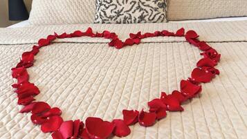A bed with a quilted bedspread and a heart-shaped arrangement of red rose petals.