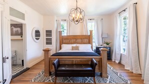 A bedroom with a wooden bed, a bench, a chandelier, and a view of the outdoors.