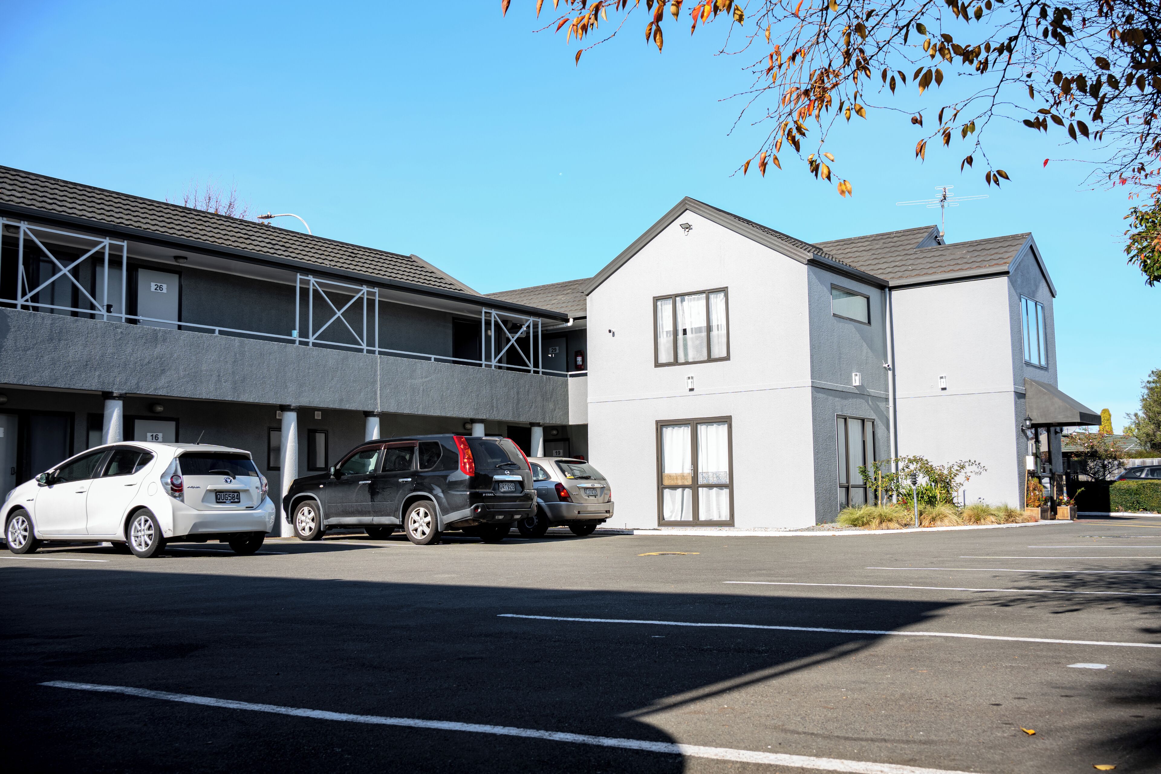 Un estacionamiento con varios coches aparcados frente a un edificio de diseño arquitectónico moderno, con techo plano y grandes ventanales.
