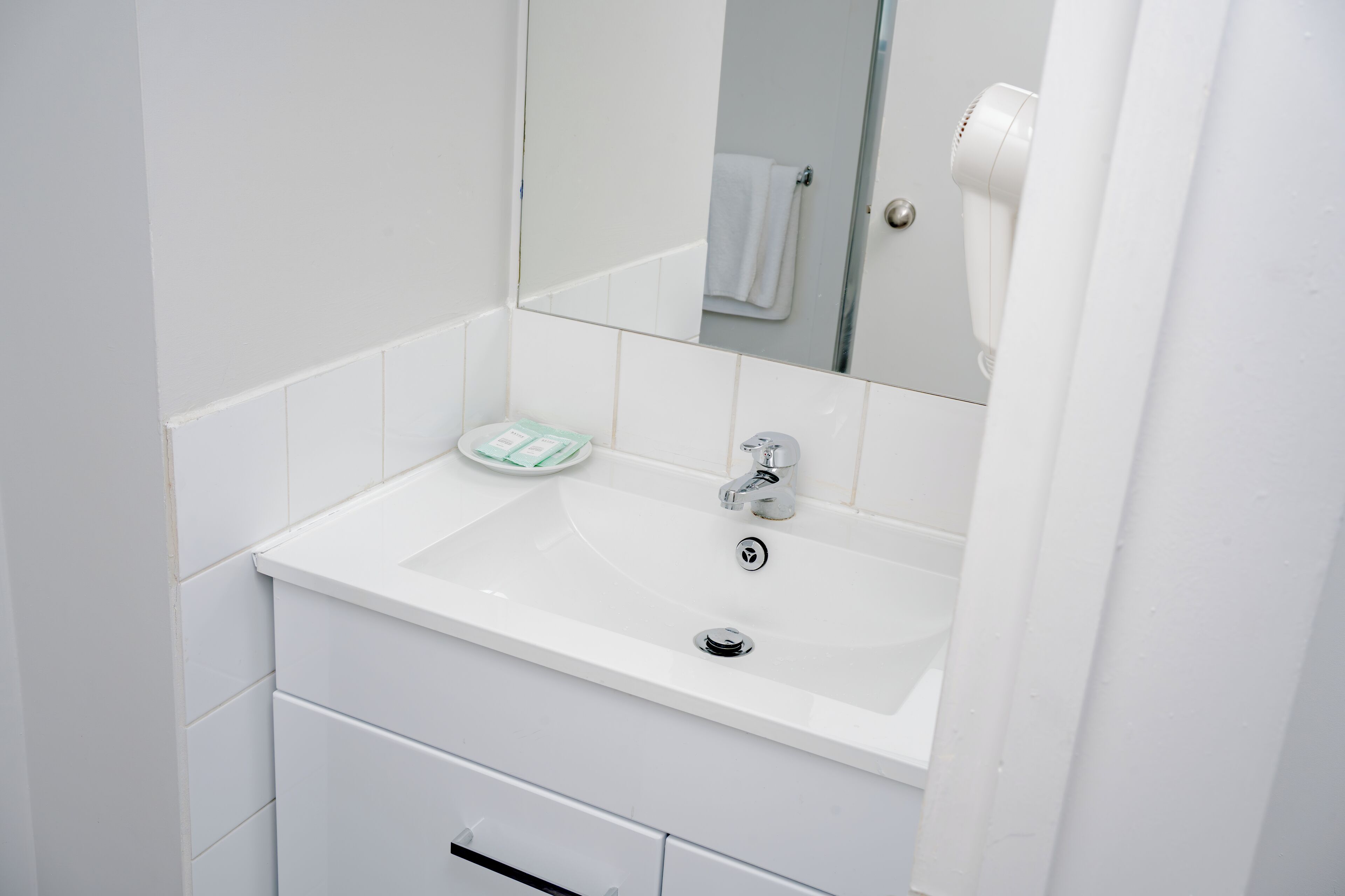 A white bathroom with a sink, mirror, and a towel rack.