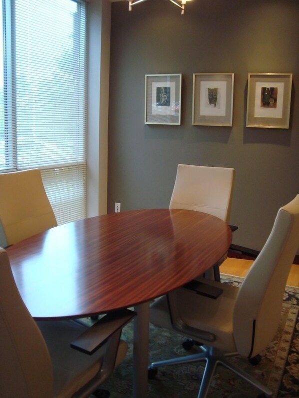 Conference room with a round table and four chairs, featuring a neutral color palette and framed artwork.
