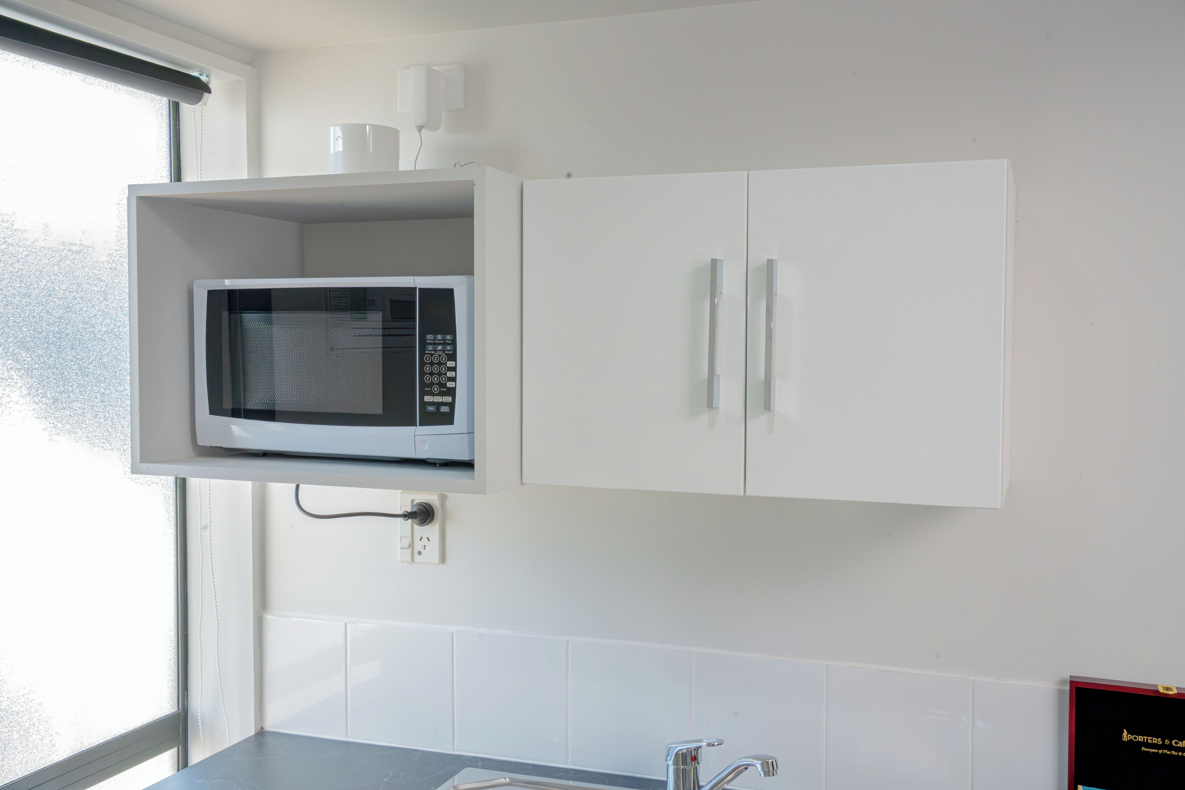 Una cocina con microondas integrado, armarios blancos y un ventanal.