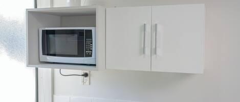 Una cocina con microondas integrado, armarios blancos y un ventanal.
