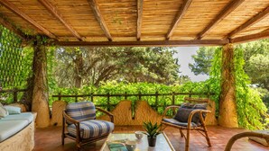 An outdoor seating area with wicker furniture and a bamboo ceiling, surrounded by lush greenery.