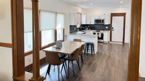 A modern kitchen with white cabinets, a central island, and a dining area with a table and chairs.