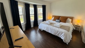 A hotel room with a bed, bedside lamps, a TV, and a window with curtains.