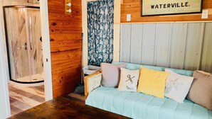 A room with a wooden wall, a glass shower enclosure, a light blue sofa with decorative pillows, and a sign reading "WATERVILLE." - Nauti Hookers, deep water access in Steinhatchee with a boat slip, cold AC, WiFi (Steinhatchee)