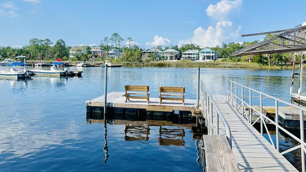 A wooden dock with benches extending into calm water, surrounded by houses and boats. - Nauti Hookers, deep water access in Steinhatchee with a boat slip, cold AC, WiFi (Steinhatchee)