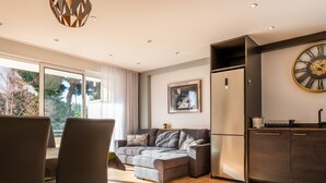 A modern living room with a sofa, chairs, a dining area, and a kitchen with a clock.