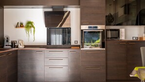 A modern kitchen with dark wood cabinets, a built-in oven, and a large window overlooking a garden.