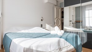A modern hotel room with a large bed, a wardrobe, a mirror, and an air conditioning unit.