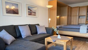A modern living room with a sofa, a small table, and a bed in the background.