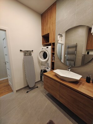 A modern bathroom with a built-in washing machine, a large mirror, and a wooden vanity with a sink. - CITY CENTER 2! A Cozy and Modern 2BR in the city center near New York Cafe! (Budapest)