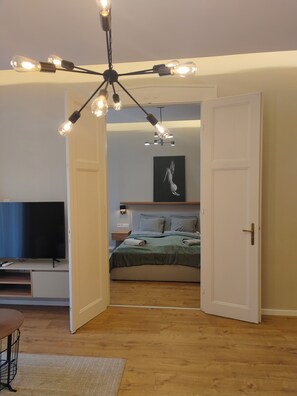 A modern bedroom with a bed, bedside tables, a TV, and a ceiling light fixture. - CITY CENTER 2! A Cozy and Modern 2BR in the city center near New York Cafe! (Budapest)