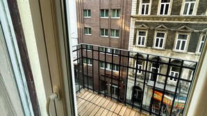 A balcony with a wooden floor, a black metal railing, and a view of adjacent buildings. - CITY CENTER 2! A Cozy and Modern 2BR in the city center near New York Cafe! (Budapest)