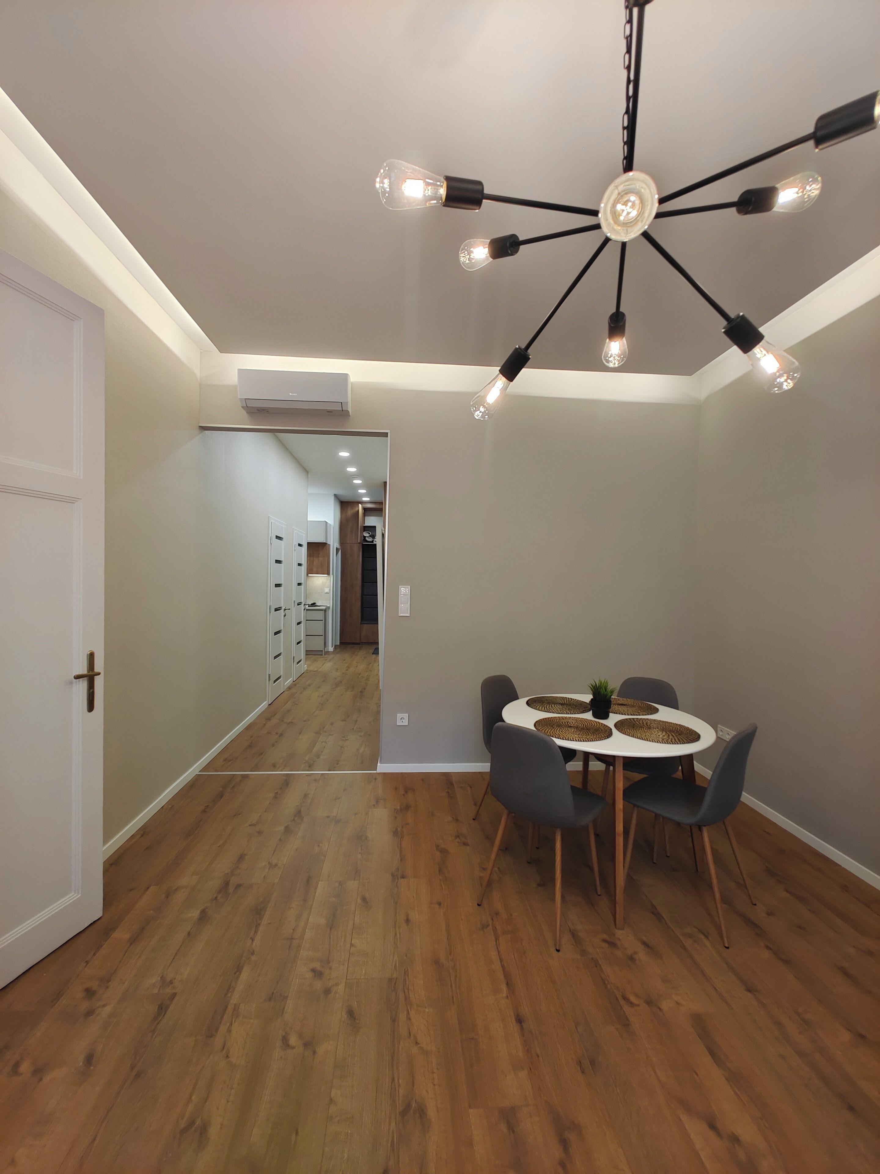 Un espace repas moderne avec une table ronde, des chaises grises et un luminaire au plafond au design original.