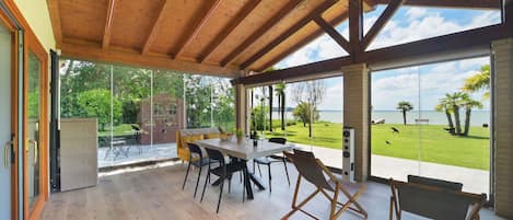 Tilava patio, jonka katto on tehty puusta, siinä on ruokapöytä tuoleineen, ja sieltä on näkymä vehreälle alueelle ja vesistölle.
