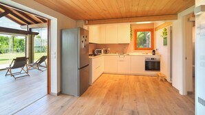 Een moderne keuken met houten vloer, witte kasten, een roestvrijstalen koelkast en een raam met uitzicht op een tuin.