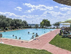 A swimming pool with people in the water, surrounded by grass and trees. - La Spiaggia by Interhome (Magione)