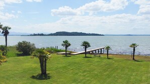 Een gazon met een houten bankje en palmbomen, met uitzicht op een waterpartij en een eiland in de verte.