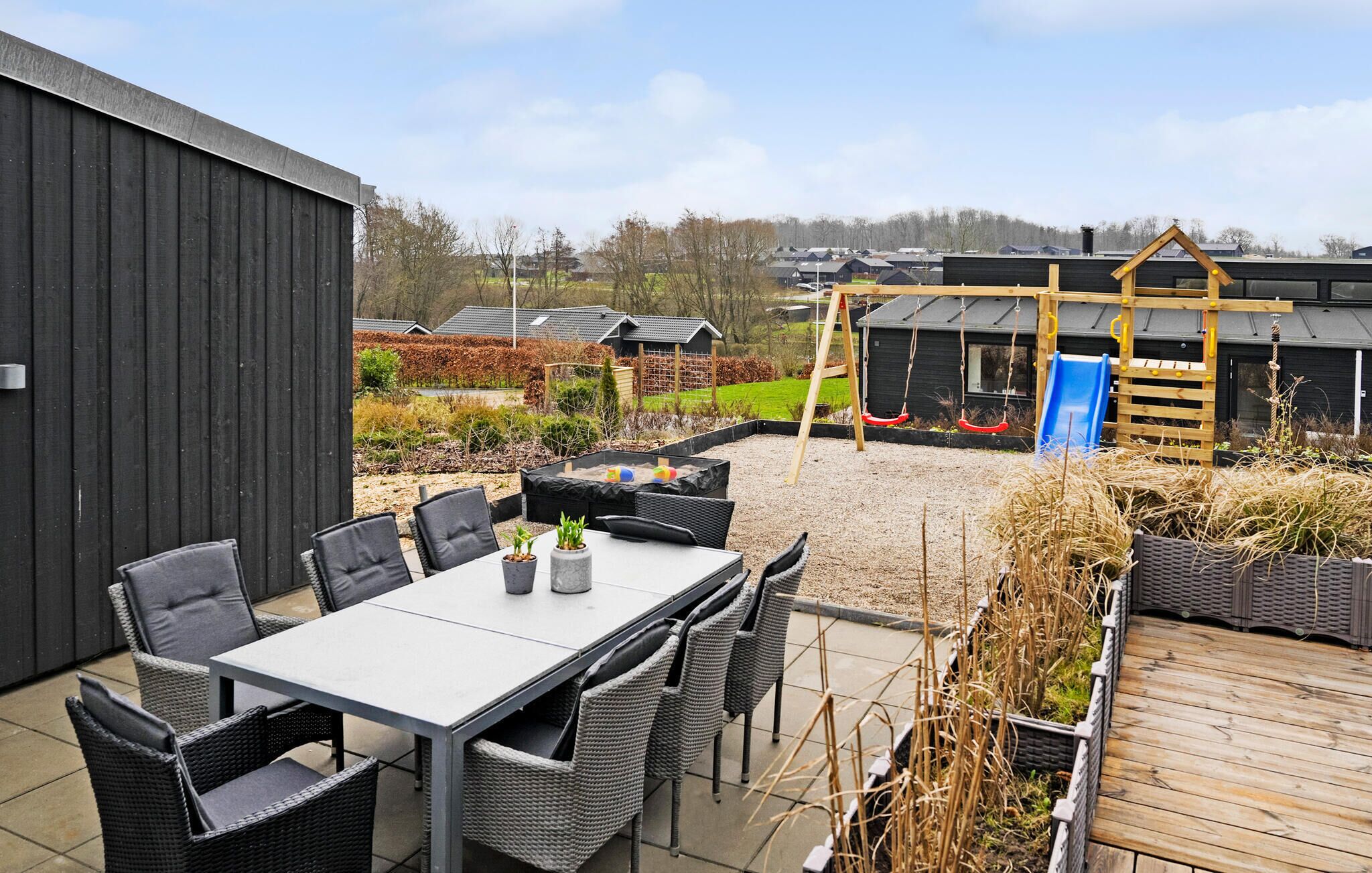 An outdoor patio with a table and chairs, a wooden deck, and a playground with a slide.