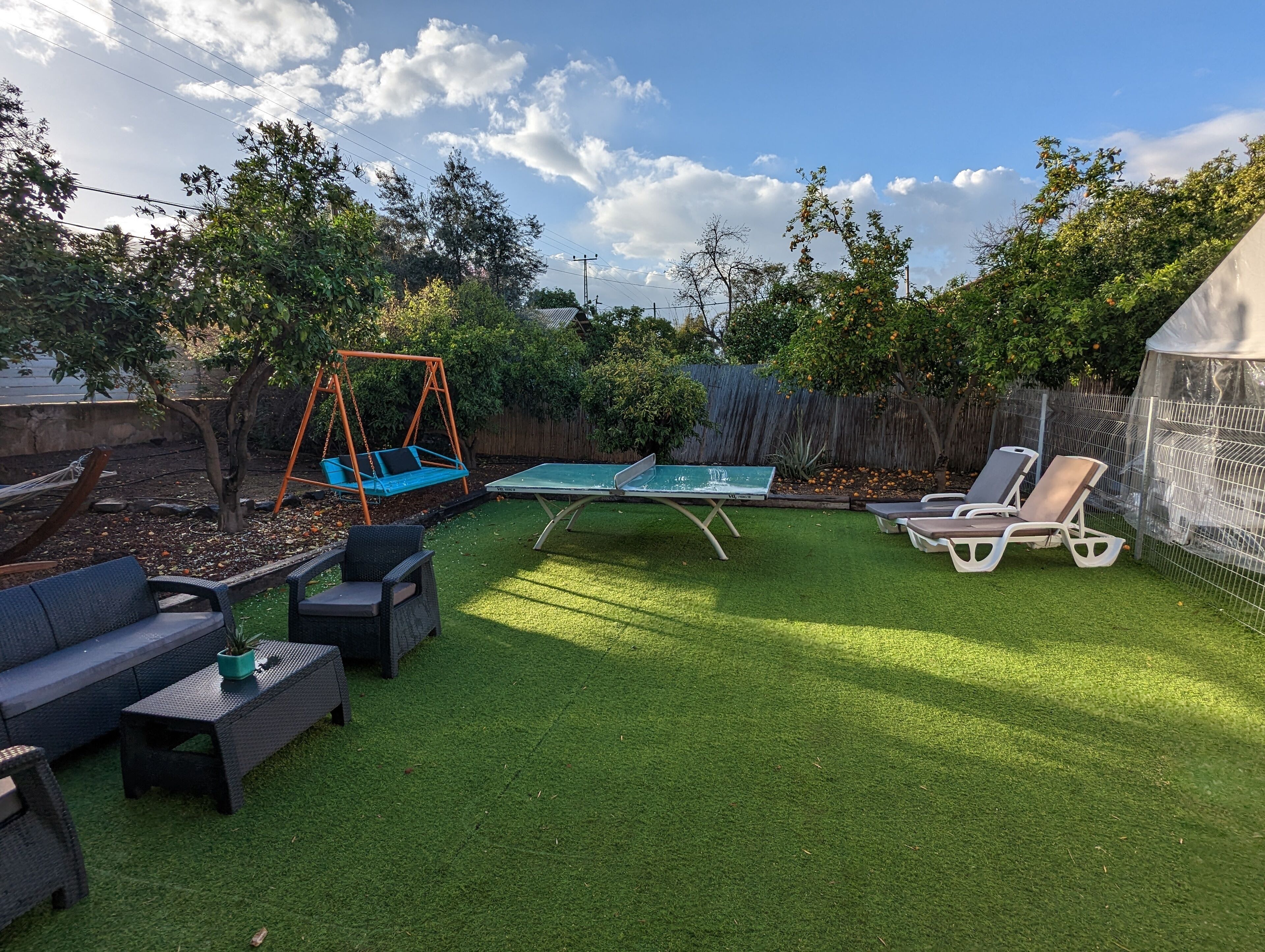 Un jardin avec une pelouse artificielle, une table de ping-pong, du mobilier d’extérieur, une balançoire et un espace abrité.