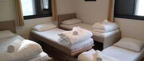 A hotel room with four single beds, each with a rolled white towel and white pillows. There is a framed picture on the wall above the beds.