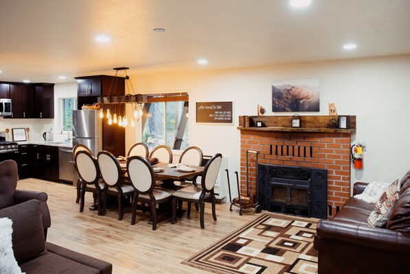 A modern kitchen with dark cabinets, a dining area with a wooden table and chairs, a fireplace, and a living room with a brown leather sofa. - Spacious 6-Bedroom Tahoe Cabin, 9 minutes to Sierra Ski Resort! Mountain Views (Twin Bridges)