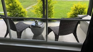 Una habitación con un ventanal grande, sillas de mimbre, una mesa de hormigón y un florero.