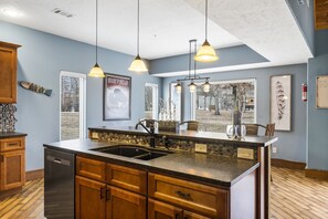 Una cucina con una grande isola, armadietti in legno, lavastoviglie integrata e illuminazione a sospensione.