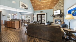 A spacious living area with a fireplace, a large sofa, and a kitchen area with wooden flooring and cabinetry. - Family-Friendly Lake Retreat, Cmty Firepits, Playground and Hot Tub, Free SDC Tickets & more! (Branson)
