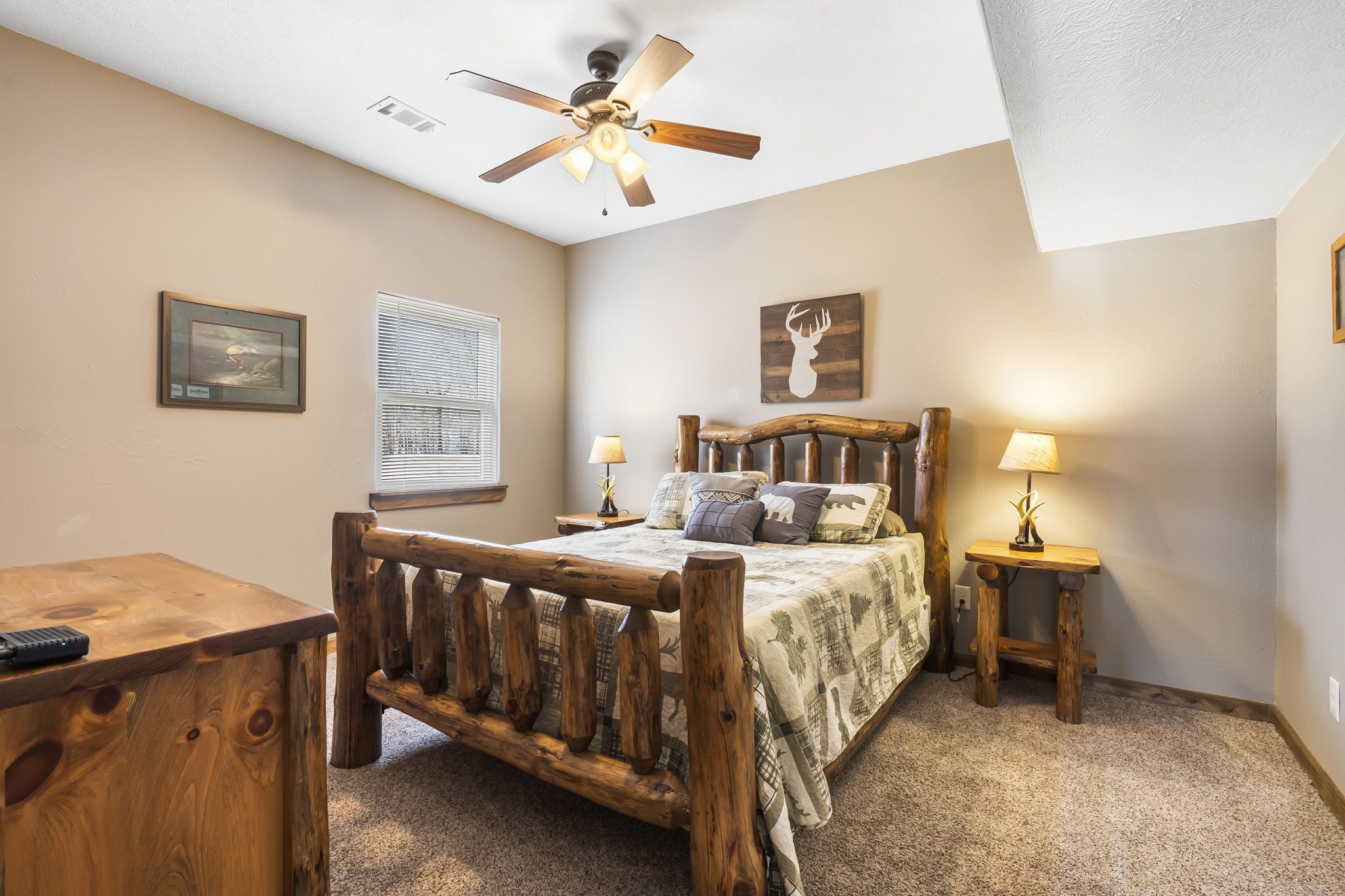 Une chambre à coucher avec un lit en bois, deux tables de chevet avec des lampes, un ventilateur de plafond et une fenêtre avec des stores.